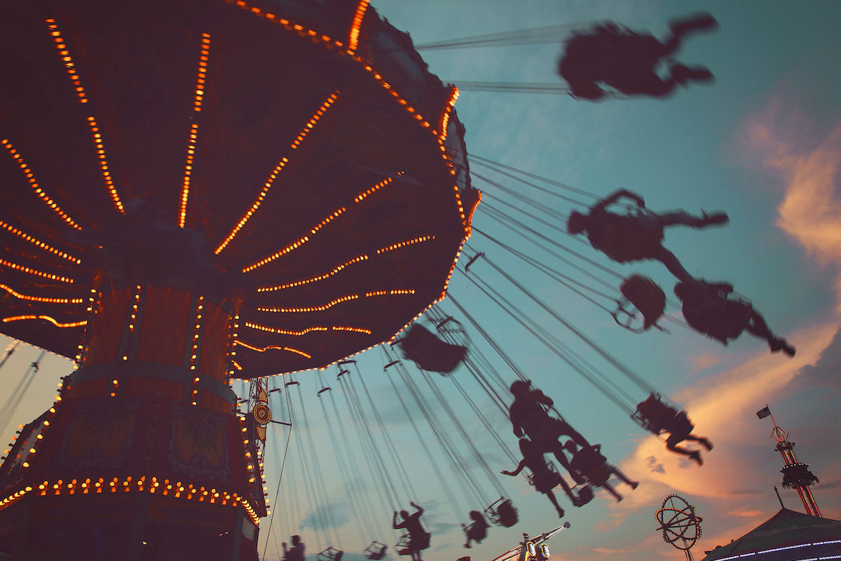 a local fair at dusk with people riding swinging rides and enjoying the summer atmosphere toned with a retro vintage instagram filter app or action